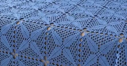 A blue crochet bedspread and matching pillow covers made with intricate lace square motifs, displayed on a neatly made bed.