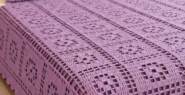 A lavender crochet bedspread and matching pillows with openwork square motifs and a scalloped border on a neatly made bed.