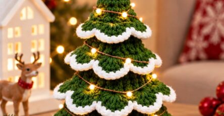 A crochet Christmas tree with green scalloped layers edged in white and topped with a yellow crochet star, decorated with LED string lights.