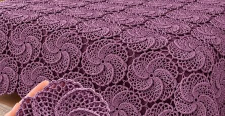 Lavender-colored crochet bedspread with repeating swirl motifs covering a bed, matching decorative pillows, and a close-up of one motif held in hand.