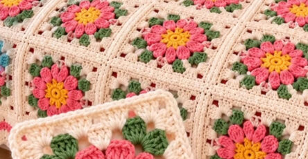 Colorful crochet blanket with floral granny squares in yellow, pink, green, and cream, displayed on a bed with one square shown up close.
