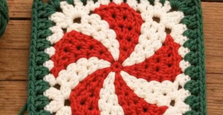Crocheted square featuring a red and white swirl motif resembling a peppermint candy with a green granny square border.