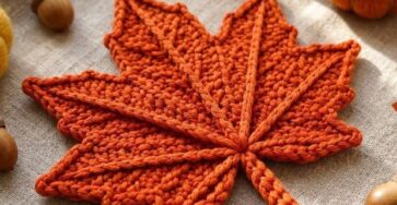A flat, bright orange crochet maple leaf with textured veins, displayed as an autumn-themed decoration.