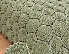 A soft green crochet bedspread made of leaf motifs joined together, covering a bed with matching leaf motif pillow covers.