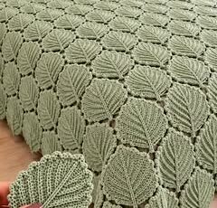A soft green crochet bedspread made of leaf motifs joined together, covering a bed with matching leaf motif pillow covers.