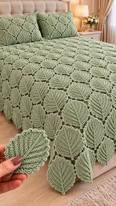 A soft green crochet bedspread made of leaf motifs joined together, covering a bed with matching leaf motif pillow covers.