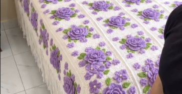Crochet bedspread and pillows with large 3D lavender roses, green leaves, textured white granny squares, and fringe edging.