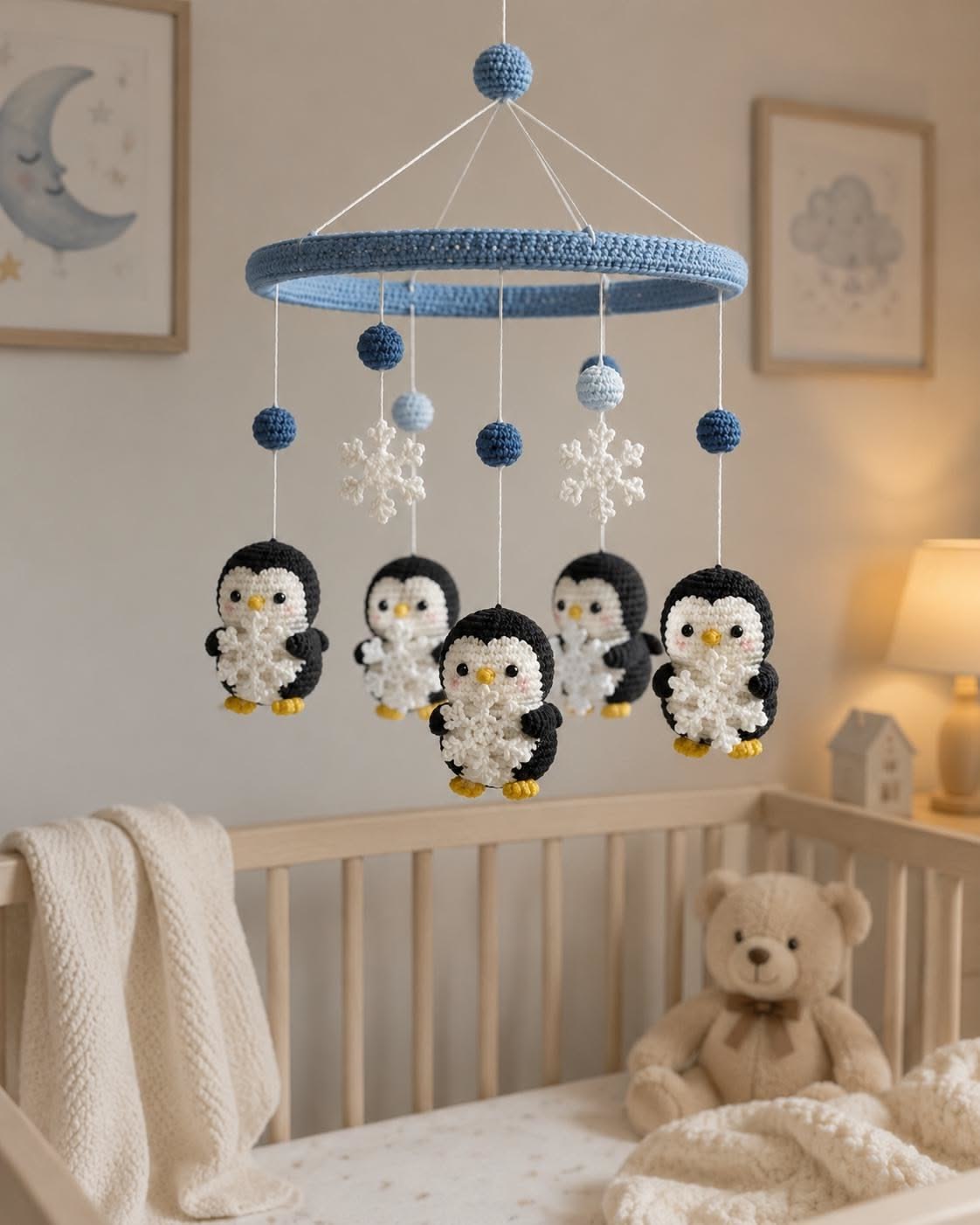 Crochet baby mobile with black and white penguins, snowflakes, and blue beads hanging from a crocheted blue ring.