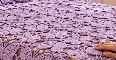 Lavender crochet bedspread, pillows, and curtain featuring large butterfly motifs connected with lace and pearl accents in a bright bedroom.