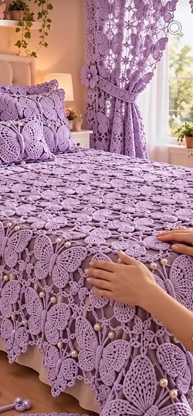 Lavender crochet bedspread, pillows, and curtain featuring large butterfly motifs connected with lace and pearl accents in a bright bedroom.