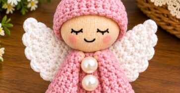 Handmade crochet angel ornament with a pink dress, white wings, soft face, and pearly buttons, designed as a tabletop or hanging decoration.