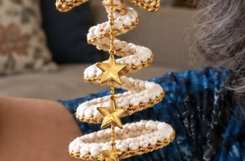 A hand-crocheted spiral Christmas tree ornament with a central gold string, golden star charms, and a crocheted star topper, featuring white textured stitches bordered in gold.