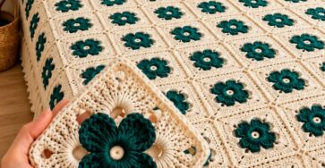 A crochet bedspread and pillow cover made from cream and teal floral granny squares, joined together and finished with tassels.