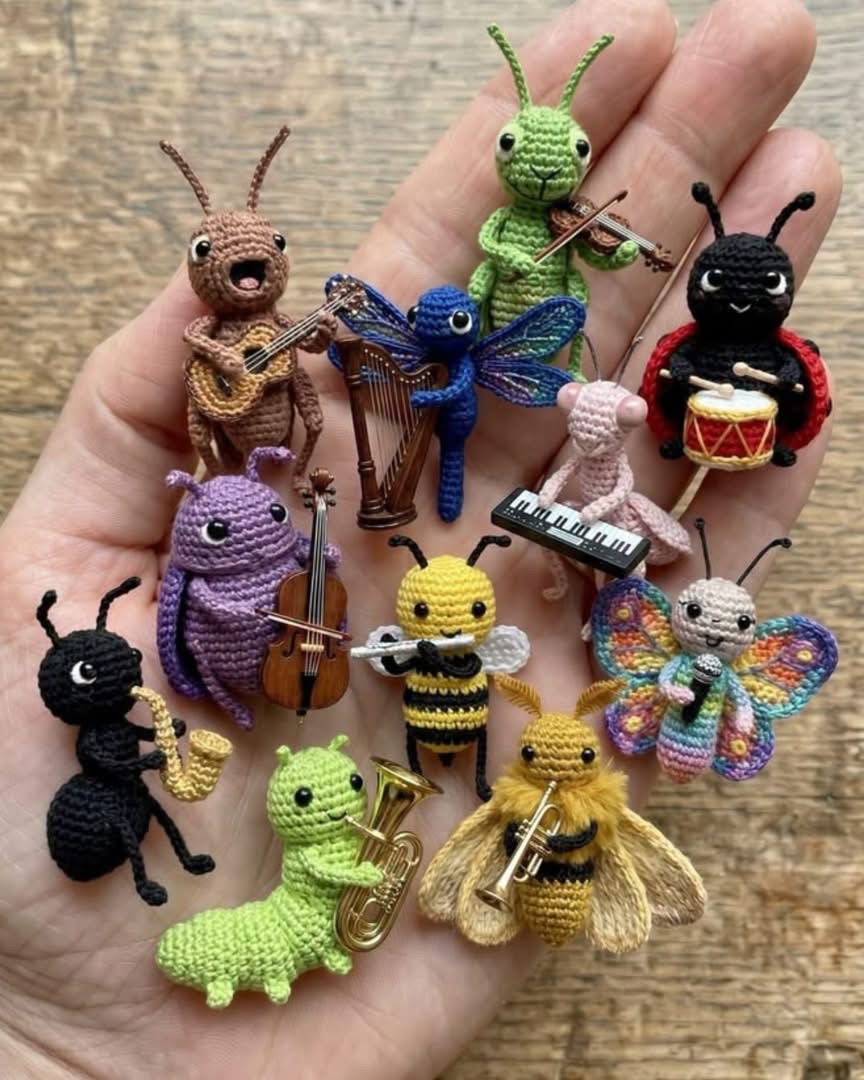 A hand holding a collection of tiny, crocheted amigurumi insects, each playing a miniature musical instrument.