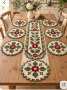 A crochet table runner and placemat set with central red flowers, green leaves, off-white and olive round motifs, arranged beautifully on a wooden table.