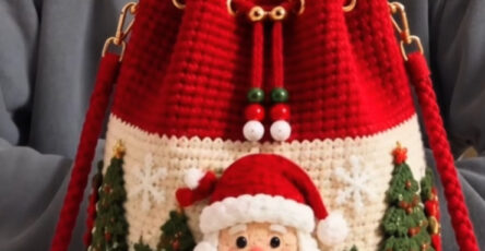 A festive crochet bucket bag with red top, cream body, 3D Santa face, Christmas trees, poinsettias, and drawstring closure.