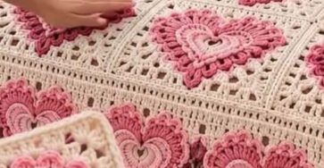 A crochet blanket and pillow set featuring granny squares with layered heart motifs in shades of pink and cream, arranged on a bed.