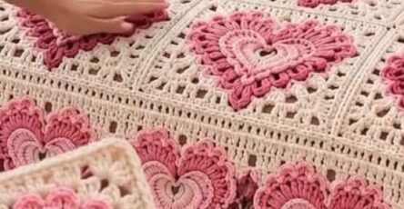 A crochet blanket and pillow set featuring granny squares with layered heart motifs in shades of pink and cream, arranged on a bed.