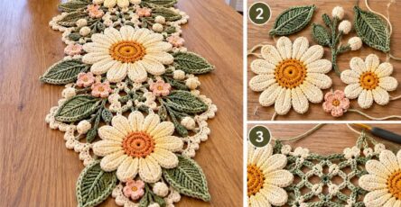 A crocheted table runner with large daisy flowers, green leaves, small blossoms and an intricate lacy border.