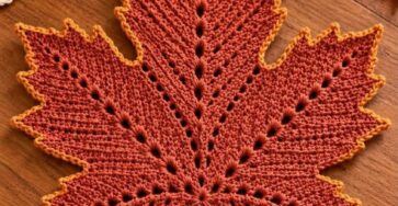 A crocheted maple leaf placemat in shades of orange and brown with pointed edges and textured veins, shaped like a real leaf.