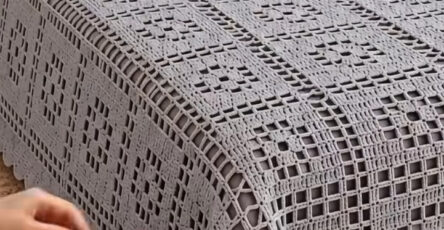 A large, elegant crochet bedspread and matching pillow covers with a geometric lattice pattern in soft gray displayed on a bed.