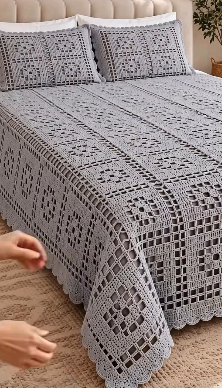 A large, elegant crochet bedspread and matching pillow covers with a geometric lattice pattern in soft gray displayed on a bed.