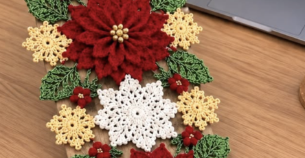 Handmade crochet table runner featuring large red poinsettias, white and yellow snowflakes, and green leaves, ideal for holiday decoration.