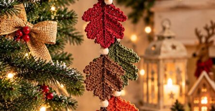 A decorative crochet garland featuring colorful autumn leaves and an acorn, hanging as an ornament on a Christmas tree.
