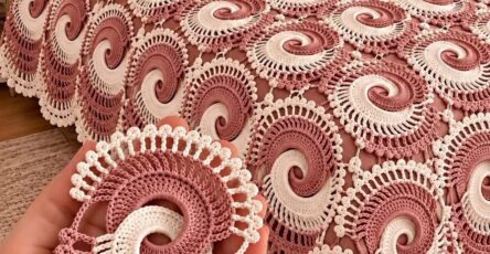Vintage-style crochet bedspread with interlocking pink and white spiral swirl motifs and decorative pillows on a bed.