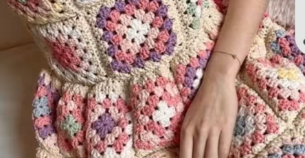 Woman wearing a handmade crochet dress made of colorful granny squares with cream borders.