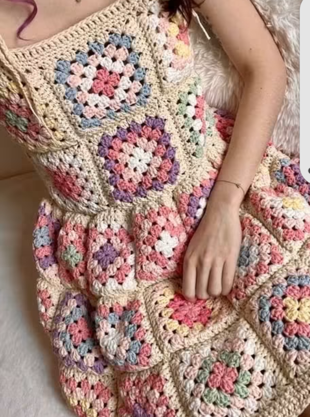 Woman wearing a handmade crochet dress made of colorful granny squares with cream borders.
