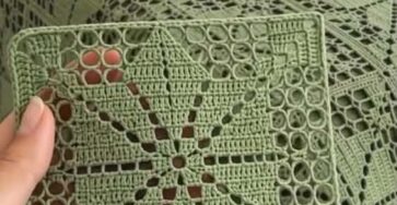 A hand holding a green rectangular crochet motif with a lacy star design, matching a larger bedspread and cushions featuring the same pattern.