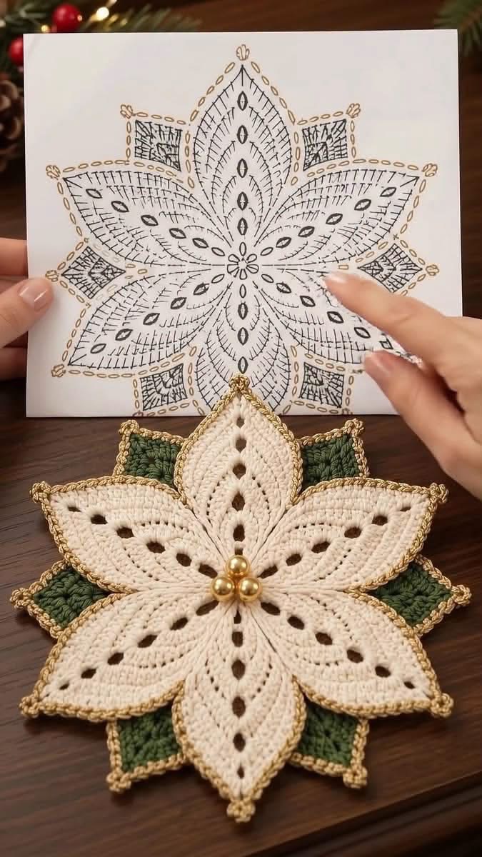 A crochet doily shaped like a poinsettia flower with white and green petals, gold edging, and golden bead accents, shown beside its drawn pattern.