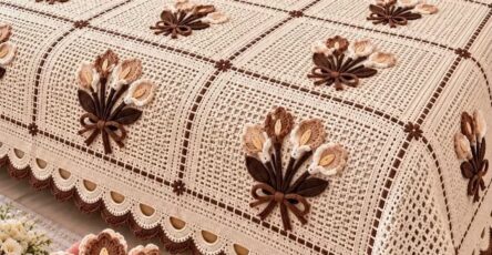 A handmade crochet bedspread with lacy granny squares, brown and beige floral bouquet appliqués, and matching pillows in a rustic bedroom setting.