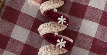 A spiral crochet Christmas tree ornament with burgundy and beige stripes, a crocheted star at the top, pearl beads, snowflake appliqués, and a bell at the base.