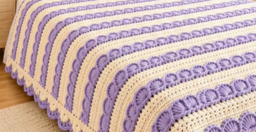 A lavender and cream striped crochet bedspread with a shell stitch texture, matching pillows, and decorative trim on a bed.