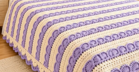 A lavender and cream striped crochet bedspread with a shell stitch texture, matching pillows, and decorative trim on a bed.