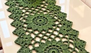 A long green crochet table runner with large floral medallion motifs joined together, featuring openwork and a scalloped zigzag border.