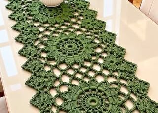 A long green crochet table runner with large floral medallion motifs joined together, featuring openwork and a scalloped zigzag border.