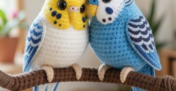 Two crocheted amigurumi budgies, one yellow and one blue, perched side by side on a branch.