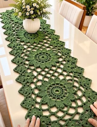 A long green crochet table runner with large floral medallion motifs joined together, featuring openwork and a scalloped zigzag border.