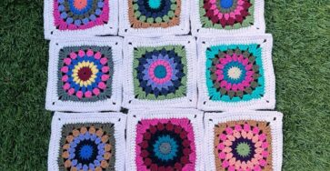 Fifteen crochet granny squares featuring colorful mandala circle centers and white borders, arranged on grass.