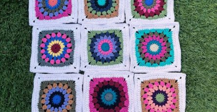 Fifteen crochet granny squares featuring colorful mandala circle centers and white borders, arranged on grass.