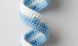 A crocheted hanging ornament of a penguin head with hat and a long, blue and white spiral tail decorated with beads and snowflake embellishments.