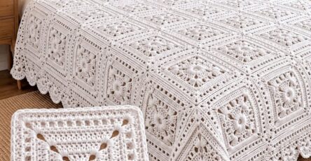 White crochet bedspread and pillows on a bed, featuring repeating daisy motif squares and intricate scalloped edging.