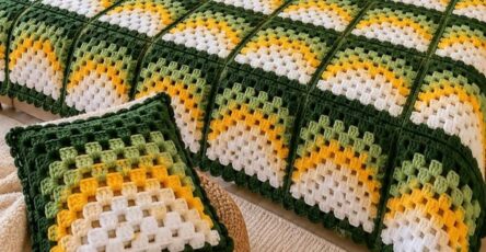 A crocheted bedspread and pillows featuring sunburst granny squares with green, yellow, and white colors on a bed.
