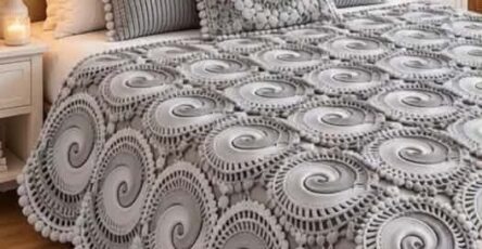 A gray spiral motif crochet bedspread with matching pillows, featuring circular swirl patterns bordered by bobbles on a neatly made bed.