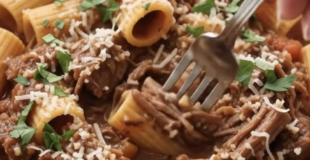 A bowl of rigatoni pasta topped with shredded beef ragù, grated Parmesan, and fresh parsley.