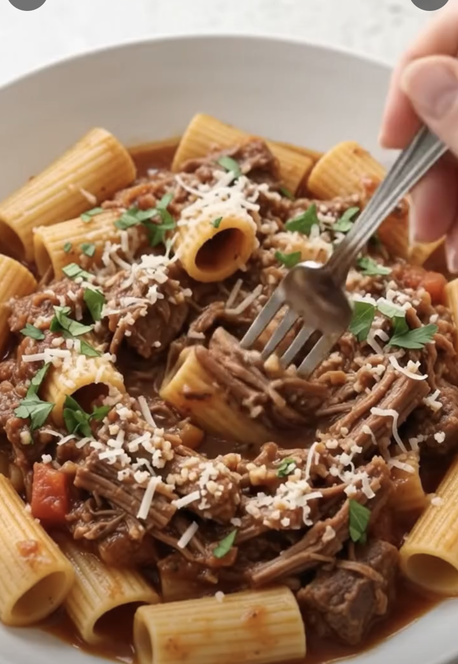 A bowl of rigatoni pasta topped with shredded beef ragù, grated Parmesan, and fresh parsley.