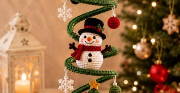 A crocheted Christmas hanging ornament with Santa, a snowman, and Christmas tree on a spiral green base, adorned with mini balls and snowflakes.